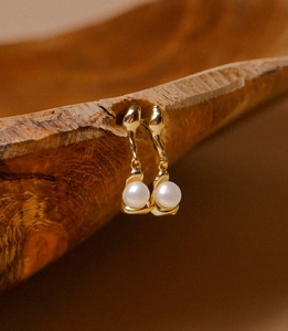 Detailed view of streamlined gold pearl earrings hanging on a rustic dark wooden vessel