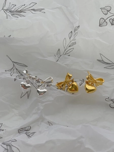 Détail de boucles d'oreilles nœud et cœur en argent et or sur un fond de papier texturé