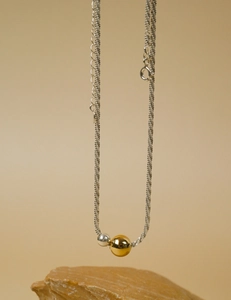 Close-up of a minimalist necklace with gold and silver polished beads on a stone