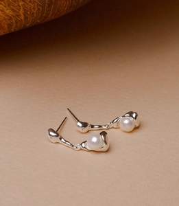 Detail of silver lava textured earrings with round white pearls on a neutral background