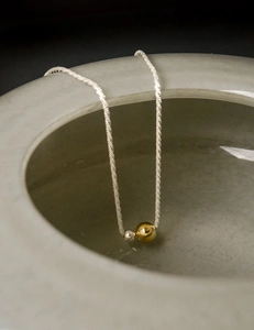 Detail of twisted silver chain necklace with gold and silver beads on ceramic bowl