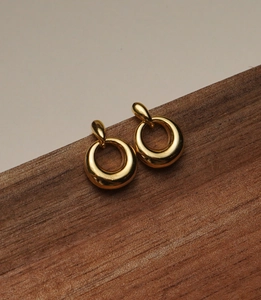 Close-up of polished gold circular drop earrings on dark wood surface with warm lighting