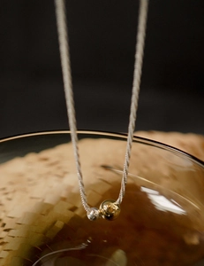 Macro detail of minimalist two-tone gold and silver beaded pendant on twisted chain