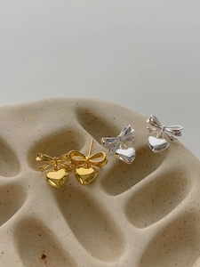 Gros plan sur les boucles d'oreilles nœuds et cœurs en or et argent sur support beige
