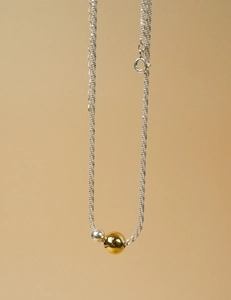 Detail of minimalist fine chain necklace featuring polished gold and silver metal beads