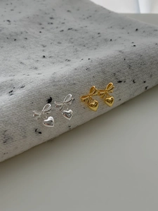 Détail macro de boucles d'oreilles nœud et cœur en argent et or sur tissu tricoté