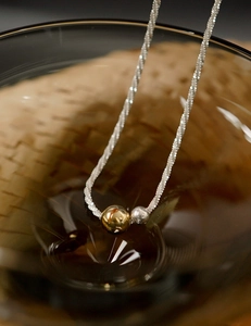 Detail of two-tone gold and silver bead necklace draped on a glass edge with soft shadows