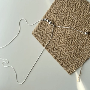Detail view of silver snake chain necklace with graduated beads on burlap texture