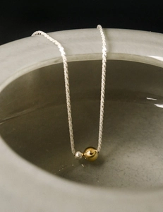 Detail of twisted silver chain with gold and silver bead pendants on a ceramic edge
