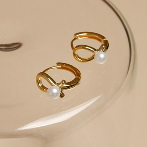 Elegant 925 silver pearl drop earrings with gold twist knot design on glass tray