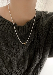 Close-up of dual-tone gold and silver beads on a twisted rope chain necklace worn on a sweater