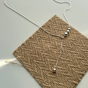 Minimalist silver snake chain necklace with gradient polished metal beads on linen texture