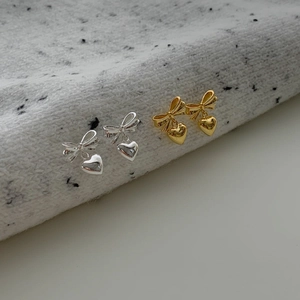 Boucles d'oreilles nœud et cœur en argent et doré sur un tissu texturé