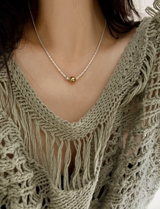 Detail of minimalist silver chain with two-tone gold and silver beads on a model