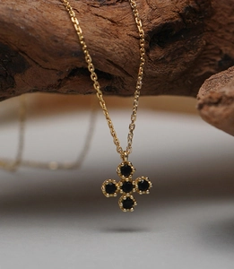 Macro shot of gold cross necklace featuring black gemstones on a rustic wooden backdrop