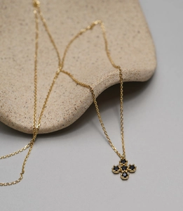 Macro shot of gold cross necklace with five black stones on a beige ceramic plate