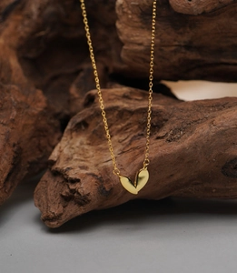 Close-up of gold heart necklace with double pendants on a textured wooden branch