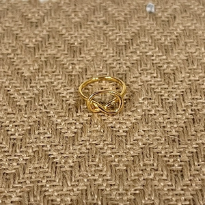 Polierter goldener Knotenring mit Infinity-Design auf rustikalem Hintergrundstoff