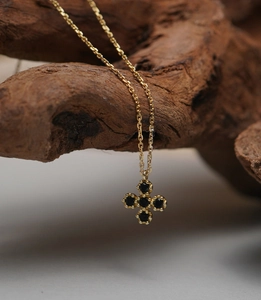 Close-up of gold clover necklace with black zircon stones hanging on a rustic wood piece