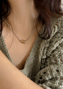 Detailed shot of two-tone gold and silver beaded pendant necklace on green knit sweater