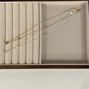 Detailed close-up of gold and silver teardrop pendant necklaces in a beige velvet jewelry box