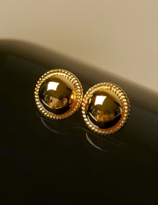 Detail of golden dome stud earrings with intricate twisted rope texture on dark surface