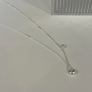 Macro detail of S925 sterling silver ball pendant necklace on a minimalist grey surface