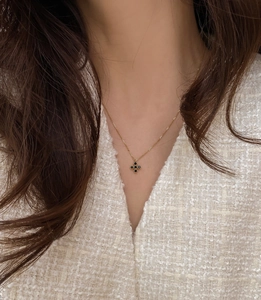 Close-up of gold chain necklace with a black four-leaf clover pendant on female model