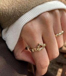 Detail of gold openwork heart ring with textured beaded band in a layered style