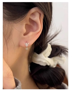 Nahaufnahme eines silbernen Mini-Schleifenohrrings am Ohr im zarten, edlen Stil