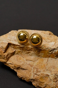 Close-up of golden dome stud earrings with rope border on natural stone background