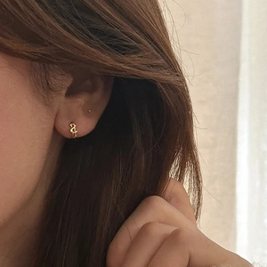 Gros plan de mini créoles dorées minimalistes avec breloque lettre sur l'oreille