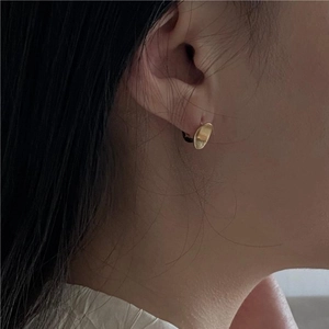 Gros plan d'une boucle d'oreille ovale dorée minimaliste portée pour montrer la taille