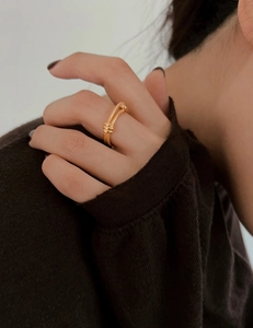 Close-up of a double-layered gold-plated knot ring with fine spiral textures on a model's finger
