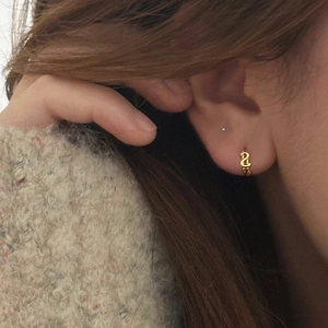 Gros plan d'une mini créole dorée torsadée portée sur le lobe de l'oreille d'un mannequin