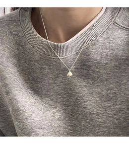 Close-up of a minimalist silver teardrop pendant necklace worn on a grey sweatshirt