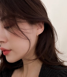 Gros plan sur une boucle d'oreille dorée avec zircon rectangulaire portée par un mannequin