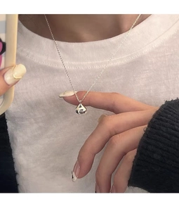 Detailed view of solid silver bean pendant necklace on a model wearing casual layers