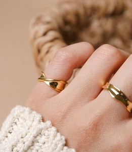 Close-up of dual gold irregular wavy rings worn by a model in a cozy knit setting