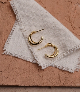 Detail of minimalist double-layered golden hoop earrings on a textured linen fabric