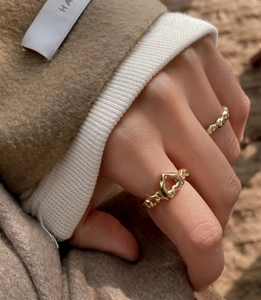 Detail of a golden heart ring with chain texture worn on hand against a warm background
