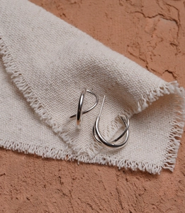 Macro shot of silver S925 knotted hoop earrings on textured fabric and terracotta wall
