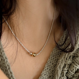 Sparkling silver chain necklace with gold and silver bead pendants worn on a green sweater