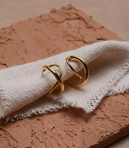 Macro detail of gold geometric criss-cross hoop earrings on textured stone and fabric