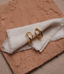 Detailed close-up of golden dual-hoop geometric earrings on textured fabric