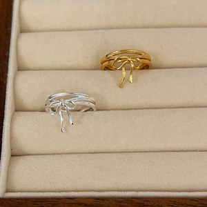 Detail of silver and gold bow ribbon rings showing layered bands on a velvet tray