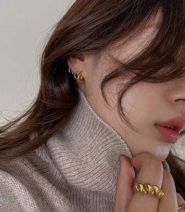 Detail of gold geometric earrings and chunky rope ring on a model in autumn knitwear