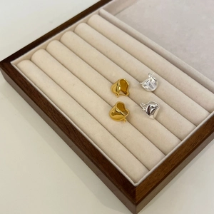 Dettaglio di orecchini minimalisti in oro e argento su espositore in velluto beige