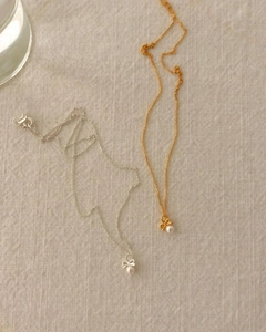Détail des colliers avec nœud et perle en versions or et argent sur tissu en lin beige