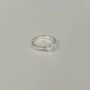 Detail view of silver bow ring with heart pendant on a minimalist cream background